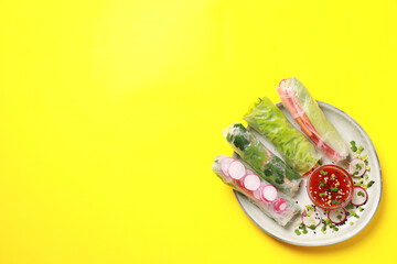 Delicious spring rolls served with sauce on yellow background, top view. Space for text