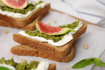 Tasty bruschetta with cream cheese, pesto sauce and fig on parchment paper