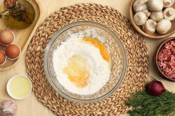Bowl with flour, eggs and ingredients on wooden table, flat lay. Process of preparing meat pie