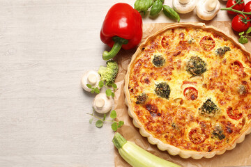 Delicious homemade vegetable quiche and ingredients on wooden table, flat lay. Space for text