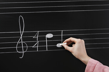 Woman writing musical notes with chalk on blackboard, closeup
