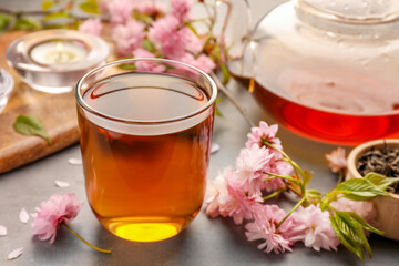 Traditional ceremony. Cup of brewed tea, teapot and sakura flowers on grey table, closeup