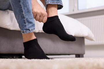 Man putting on black socks at home, closeup