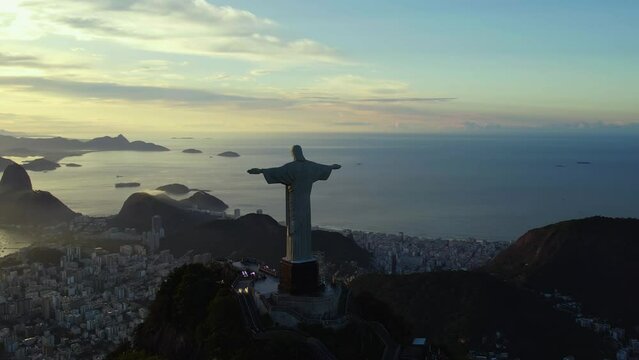 Panoramic drone shot of athe silhouette Jesus statue, overlooking the city of Rio de Janeiro, evening in Brazil