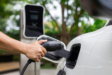 Hand inserting EV charging plug to electric vehicle in focus shot with blurred background of...