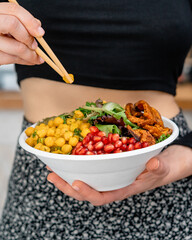 Woman eating Salad bowl in disposable plate with fresh ingredients with chopsticks. 