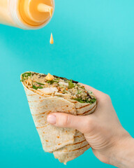 Chicken wrap in women hand seasoning with sauce on turquoise background