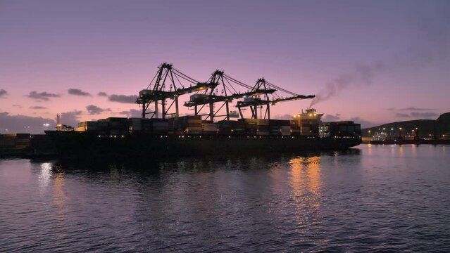Slow pan of cargo ship loading in Mexico - Ensenada during twilight.