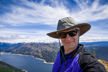 Adventurous athletic male hiker taking a selfie with a large lake and mountains in the background in the Pacific Northwest.
