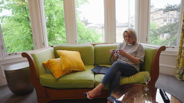 Woman sitting on sofa with orange pillows fixes her bag strap, locked off