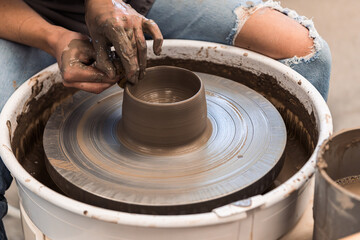 Woman working on a pottery wheel shaping the brown clay to make a bowl with both hands