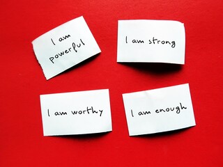 Four paper pieces on red background with handwritten text I AM STRONG, I AM WORTHY, I AM ENOUGH, I...