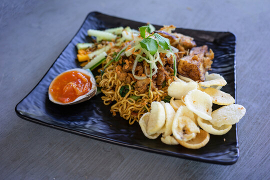 A photo of traditional Indonesian dish Mie Goreng vegetable with tempe on a black plate on a black table.