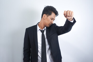 A man smells his underarm through his suit. Checking for signs of body odor from his armpit. His Antiperspirant is working. Isolated on a white background.