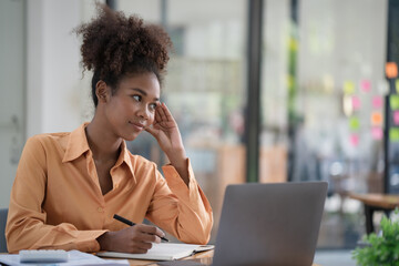 Focused young African female entrepreneur deep in thought while working at a table in a modern...
