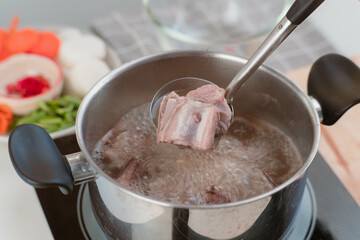 Homemade bouillon recipe. Chef's hands preparing pork rib stock (broth) with vegetables in the pot. Cook in the kitchen.