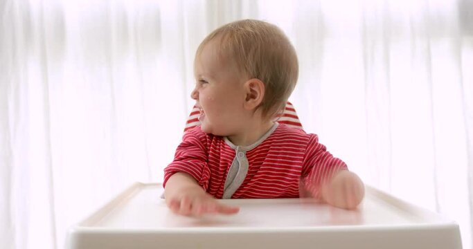 Portrait cute baby girl sitting in high chair at home. Adorable infant baby smiling happy to eat first solid food mealtime with herself BLW