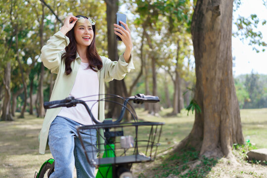 Women holding sunglasses and smiling to selfie on smartphone while cycling for exercise in the park