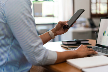 Close up of businesswoman searching business data on smartphone while working on laptop in office