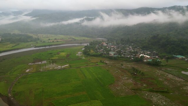 Foggy mist low clouds above village surrounded by mountain and rice field by river bend