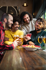 Multiracial male friends watching online videos with mobile phone while having drinks in a bar.