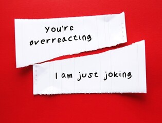On red background, torn paper with handwriting I WAS JUST JOKING, YOU'RE OVERREACTING, gaslighting...