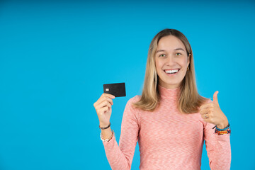 Happy young woman with thumbs up and credit card in the other hand
