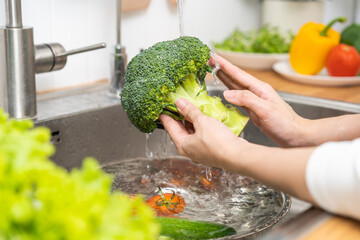 Close up asian young woman washing broccoli, tomato, carrot fresh vegetables, paprika with splash...