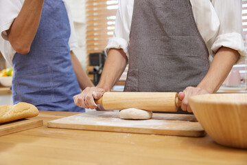 close up young man hands rolling dough with rolling pin and making a bread in the kitchen