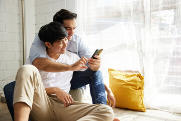 LGBT gay couple using smartphone and felling happy at home