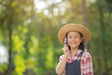Young asian girl is looking at tree leaves through magnifier, outdoor shoot, happy kid with magnifying glass, Cute little child girl looking through a magnifying glass on the grass in summer day.