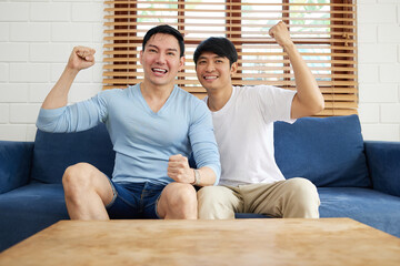 young gay couple men watching sports from television and celebrating victory pose in living room