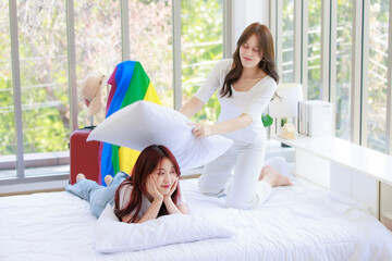 Asian young happy cheerful female LGBTQ lesbian lover couple partner holding playing pillows fight...