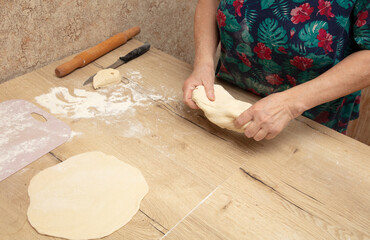 Elderly woman kneading dough on a wooden table in the kitchen