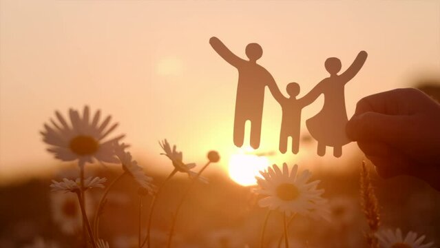 Close up of child hand holding little paper family cutout on background beautiful warm sunset, family home, foster care, world mental health day, Autism support, budgeting cost of living concept
