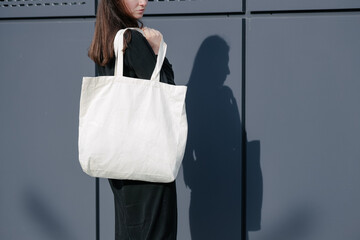 Woman holding white textile eco bag against urban city background. Ecology or environment...