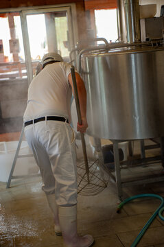 Cheesemaker cooking stirring italian bufalo organic milk in stainless steel caudrons, to produce ricotta cheese, italian food excellence worldwide export.