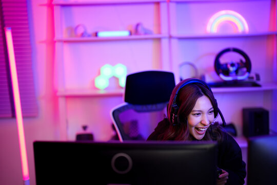 Asian e-sport woman laugh with fun emotional because of happy playing game when she live and share monitor screen on her channel and social media in entertainment gamer room with neon light