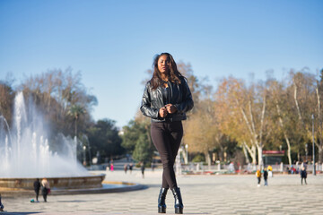 Fototapeta premium Young, beautiful, Latin and South American woman in leather jacket and top, jeans and platform shoes, clutching the lapels of the jacket posing independent and empowered. Concept beauty, diversity.