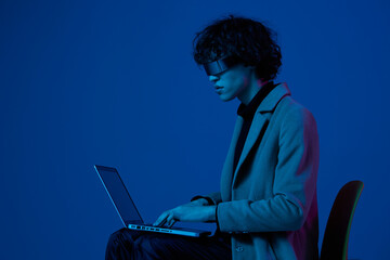 Man hacker sitting on chair with laptop and futuristic glasses in blue light, cyber security