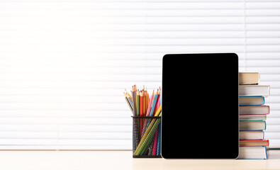 Tablet with colorful pencils and stack of books