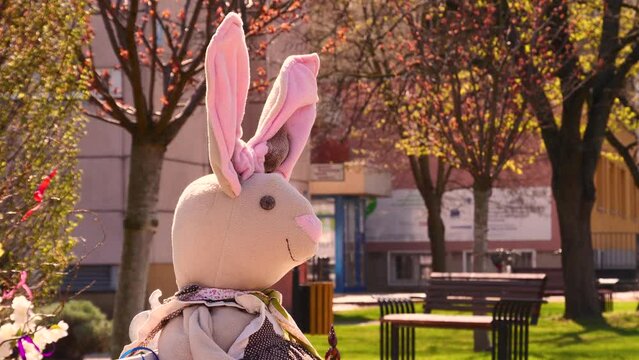 Happy Easter in spring season with rabbit decoration on a white bench. Colorful blurred background includes trees, green grass, and  Hospital building in Mosonmagyar&oacute;v&aacute;r, Hungary .