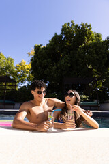 Biracial young couple having lemonade and laughing while standing in swimming pool, copy space