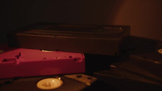 a stack of VHS cassettes stand randomly in the light of a night lamp