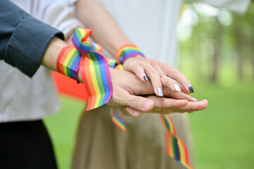 Close-up image of diverse friends putting their hands with an LGBT bracelet together.