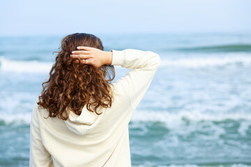 View from the back a woman with curly hair looks at the sea