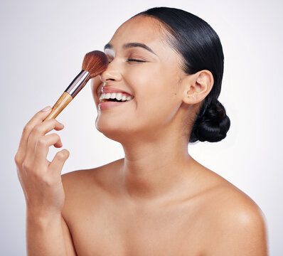 Face, makeup brush and beauty of a woman in studio for skin glow, dermatology and cosmetics. Happy female model laugh with cosmetic tools in hand for self care and facial shine on a white background