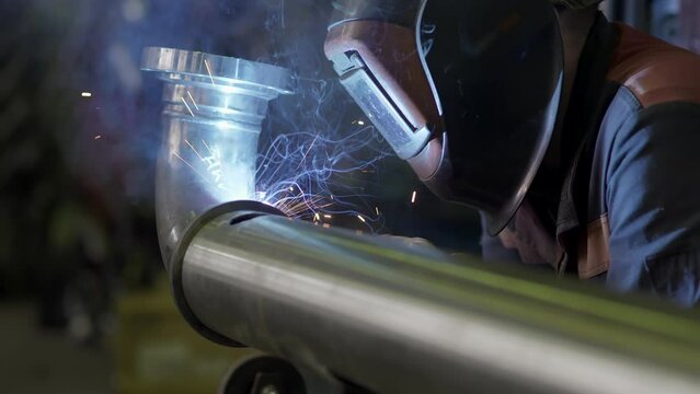 Welding work close-up. Welder worker weld pipe in protective helmet. Sparks fly out. Welding shop at Construction of Oil, Natural Gas and Fuels Transport Pipeline. Industrial Manufacturing Factory