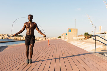 African man jumping rope on a beach. Young athlete man training outside.