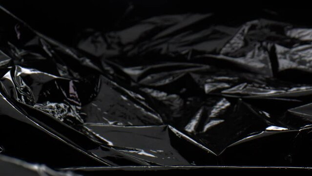 Push-in close-up of creased black plastic garbage bag, no people